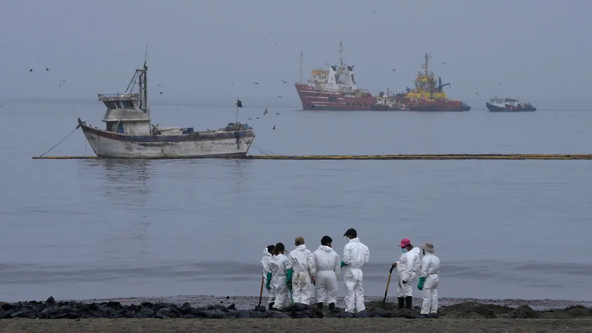 20.01.2022, Peru, Ancon: Arbeiter in Schutzanzügen reinigen Ölverschmutzten am Conchitas-Strand. Der Ölteppich soll durch einen Unfall die Küsten Perus erreicht haben. Dieser wiederum sei durch die Wellen eines unterseeischen Vulkans in der südpazifischen Nation Tonga verursacht worden. Foto: Martin Mejia/AP/dpa +++ dpa-Bildfunk +++