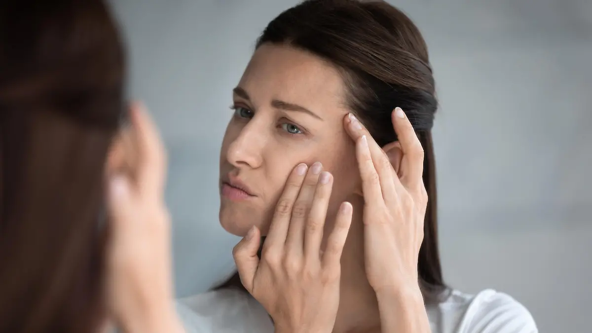Close up reflection 35s woman touches face skin looks at mirror feeling worried about first wrinkles and age-related changes derma problems. Cosmetic facial plastic surgery skincare treatments concept