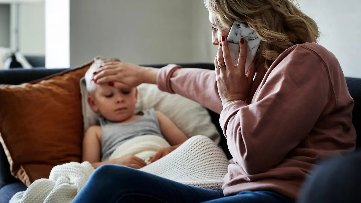Shot of a mother wearing a surgical mask making a phone call while aiding to her sick young son at home
