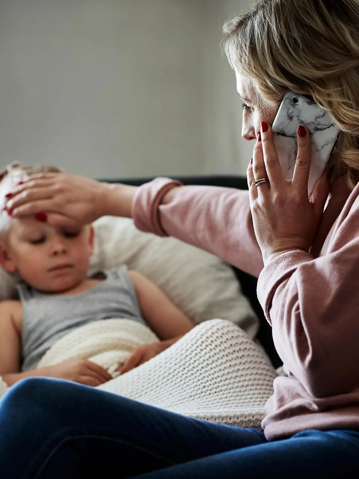 Shot of a mother wearing a surgical mask making a phone call while aiding to her sick young son at home
