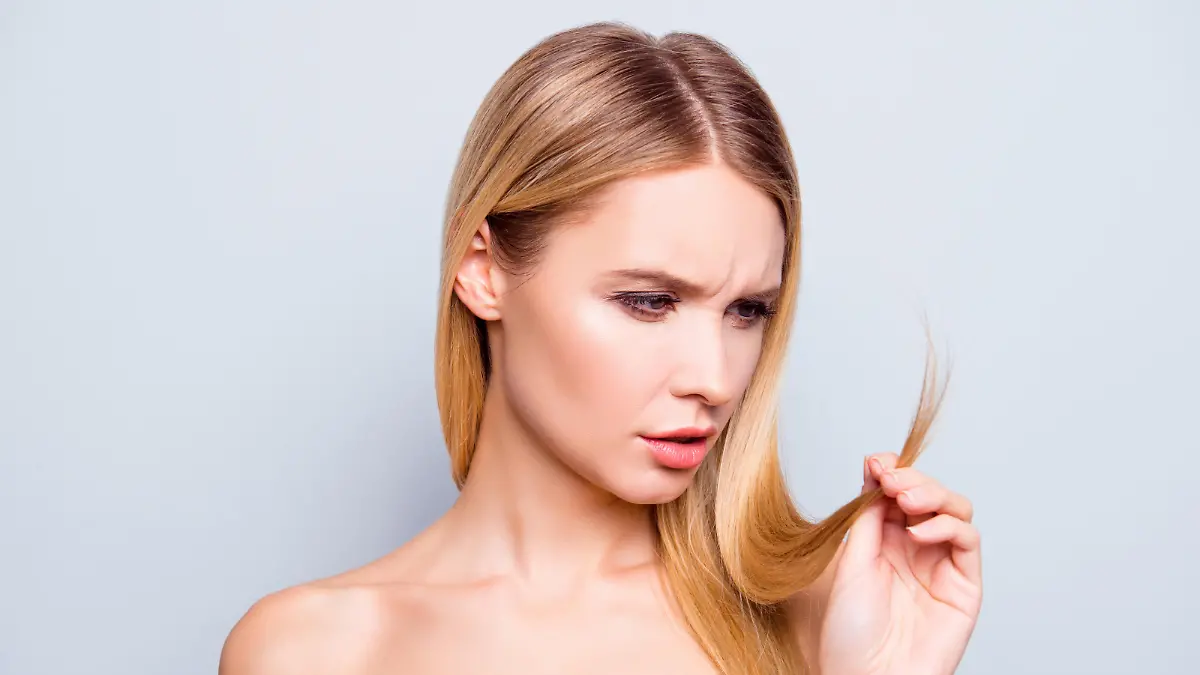 Frau schaut auf sprödes blondes Haar.
