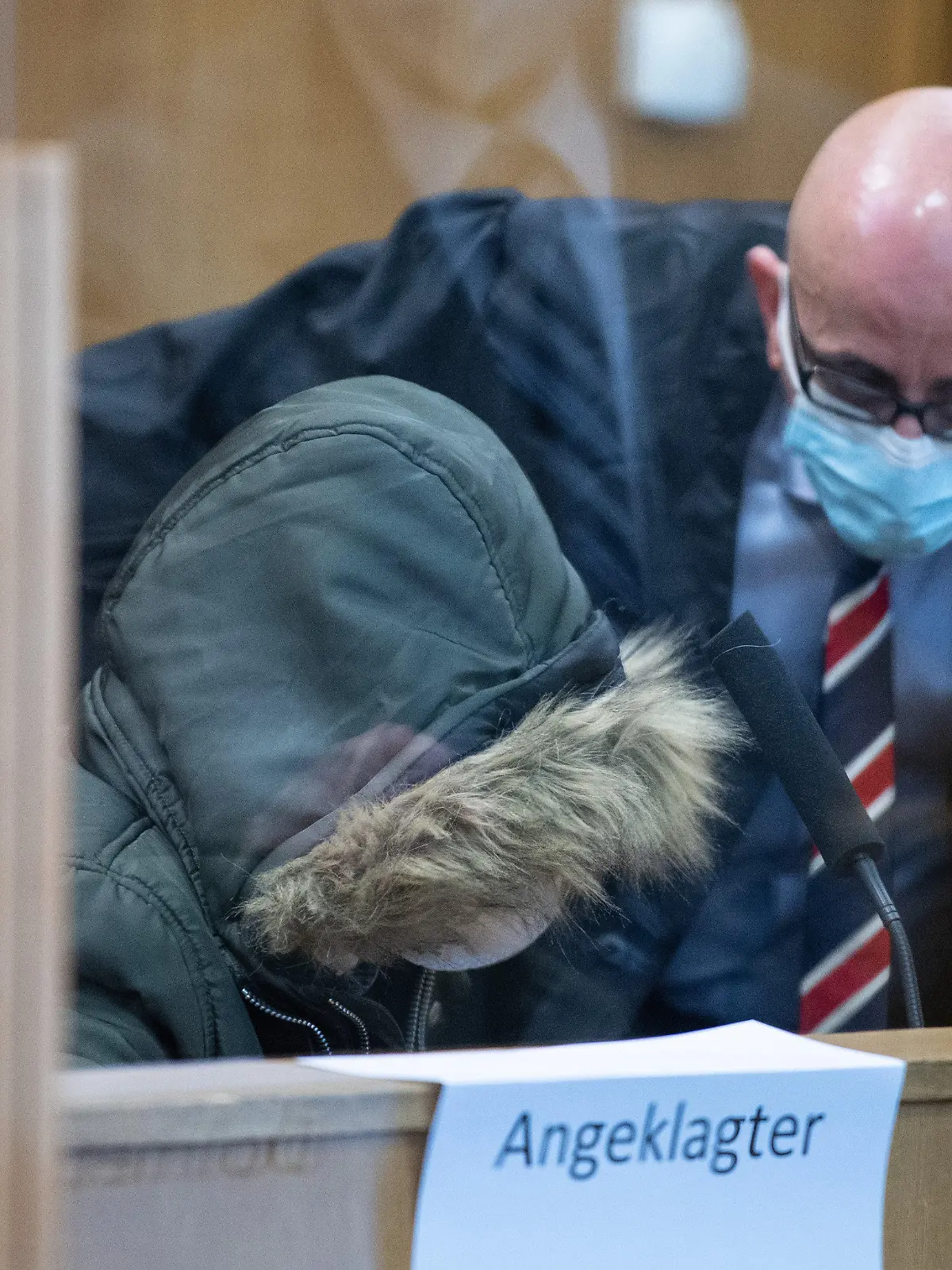 19.01.2022, Hessen, Frankfurt/Main: Der aus Syrien stammende angeklagte Arzt (l, vorne) sitzt im Sicherheitssaal des Oberlandesgerichts in Frankfurt und redet mit seinem Anwalt Oussama Al-Agi. Vor dem Oberlandesgericht beginnt am Mittwoch ein weiterer Prozess wegen Verbrechen gegen die Menschlichkeit im Bürgerkriegsland Syrien. Angeklagt ist ein 36-jähriger Arzt. Die Bundesanwaltschaft wirft ihm Folter und die vorsätzliche Tötung eines Gefangenen vor. Er soll in den Jahren 2011 und 2012 in einem Armeekrankenhaus und einem Gefängnis des Militärgeheimdiensts in Homs Gefangenen schwere körperliche sowie seelische Schäden zugefügt haben. Foto: Boris Roessler/dpa Pool/dpa +++ dpa-Bildfunk +++