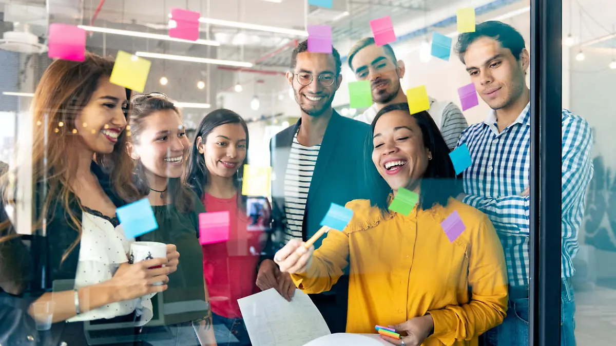 Young professionals planning tasks on glass wall with adhesive notes in co-working office