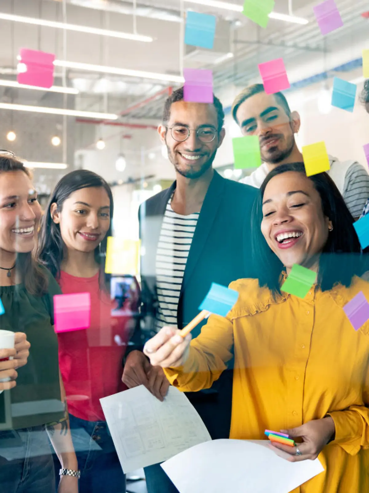 Young professionals planning tasks on glass wall with adhesive notes in co-working office