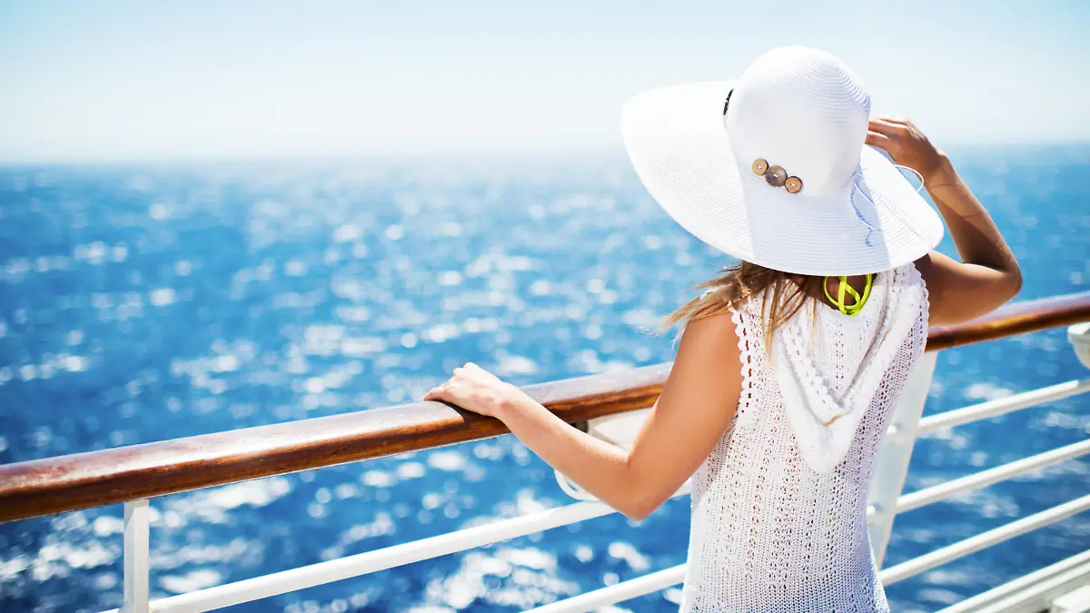 Unrecognizable woman with hat on a cruise ship looking at the view.