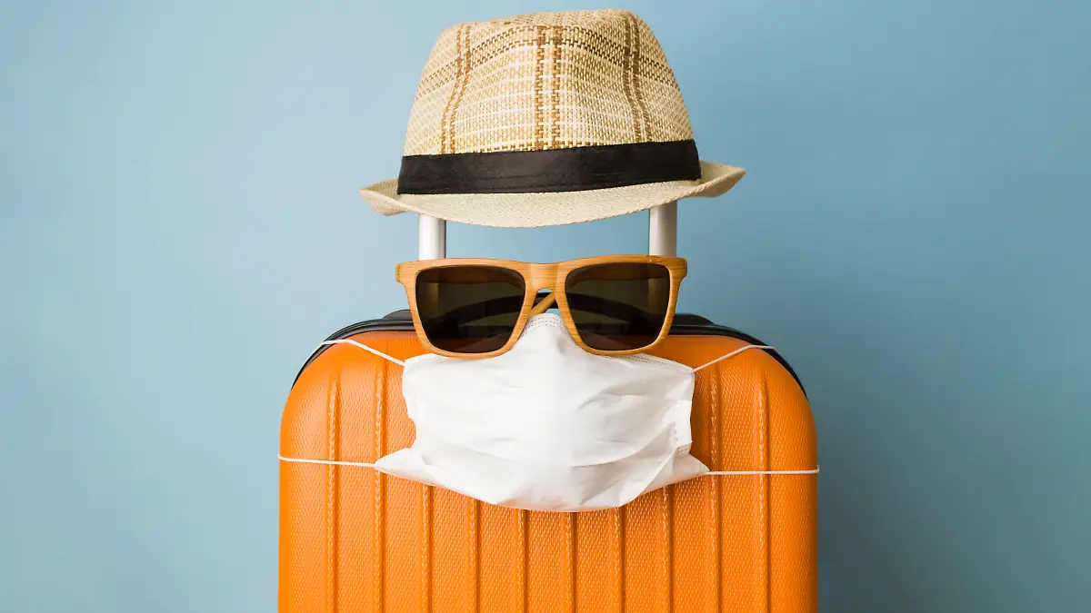 Travel restriction abstract made of tourist in form of of luggage with face mask, sunglasses and hat.