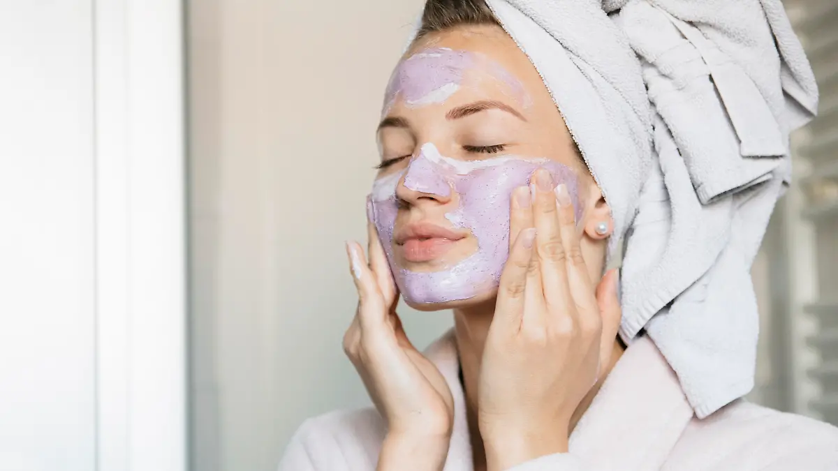 Attractive young woman putting on a beauty mask, applying it on her face