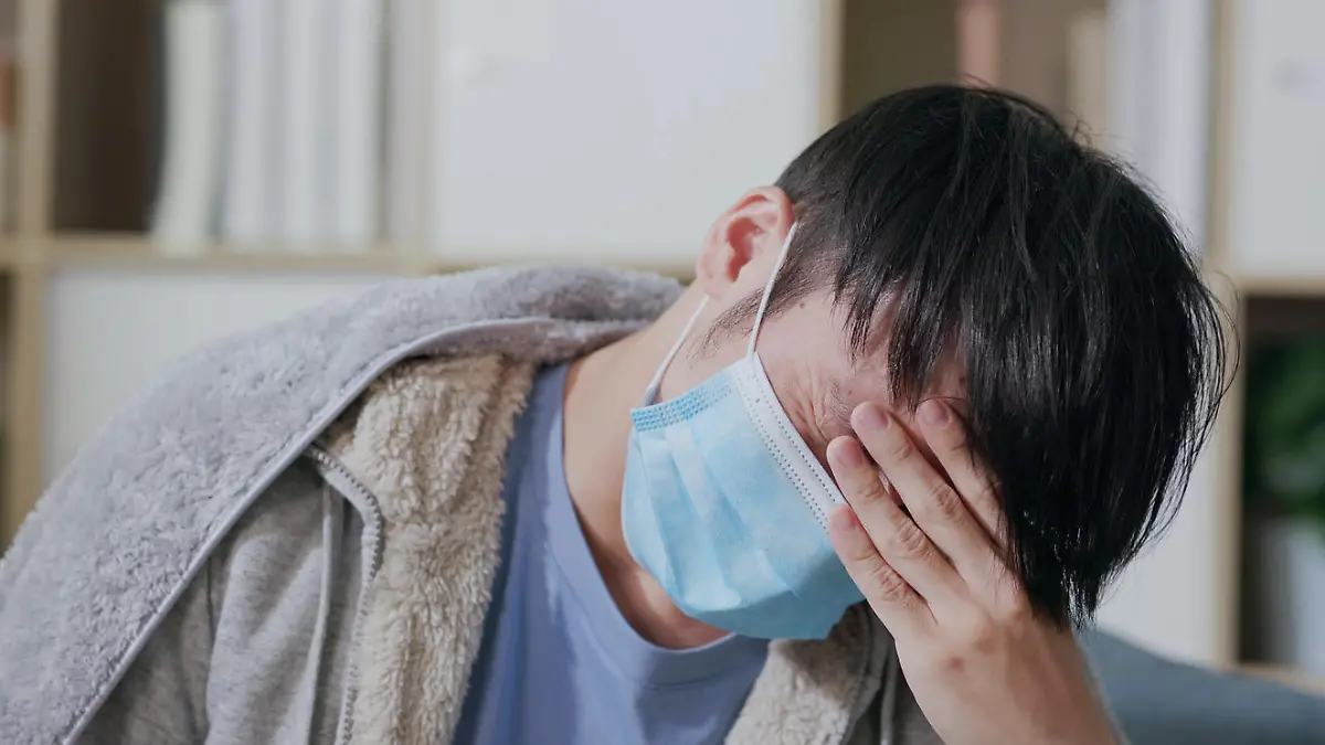 close up of sick asian man wearing face mask has headache or fever on sofa and feeling uncomfortable in living room at home