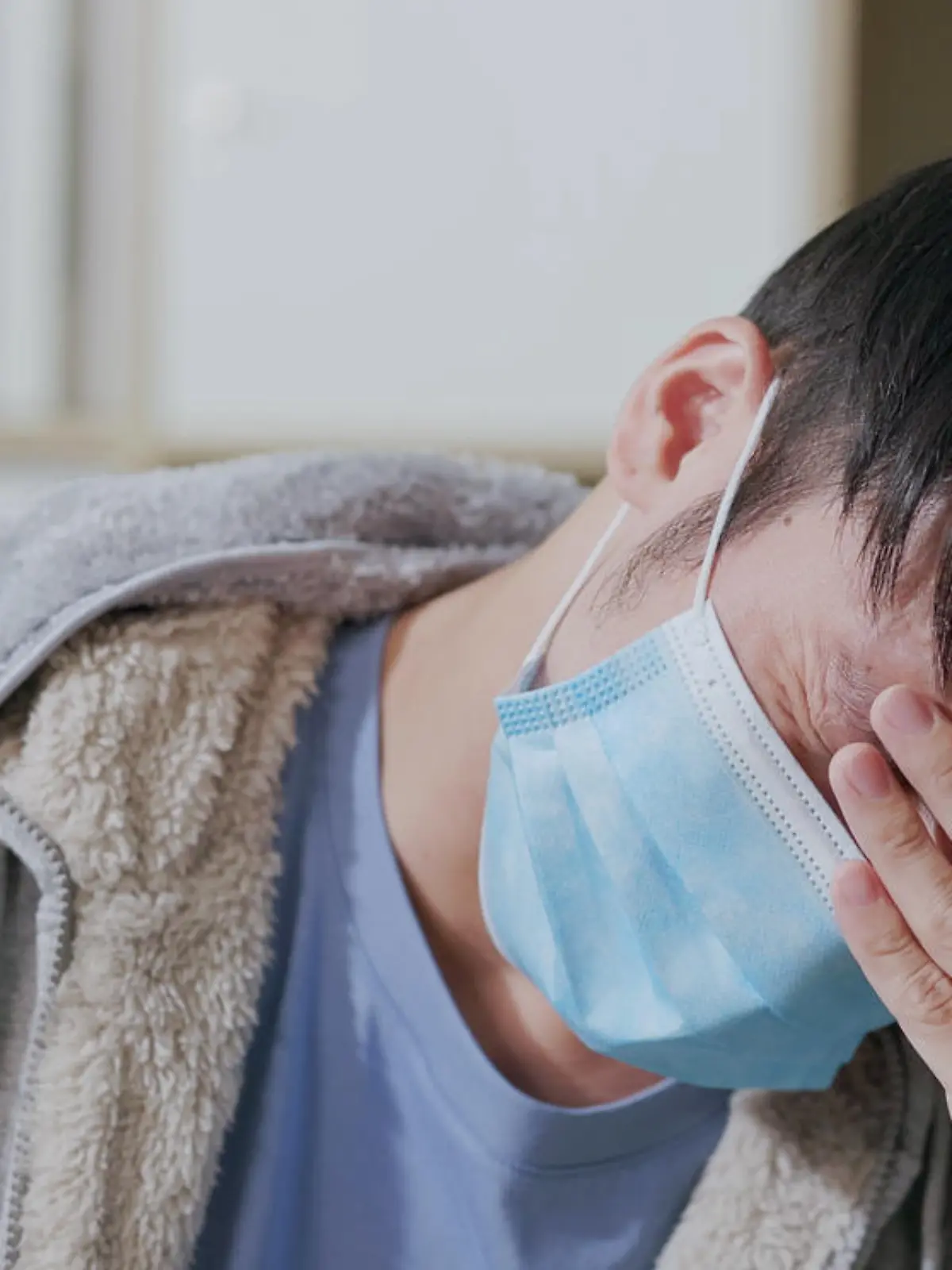 close up of sick asian man wearing face mask has headache or fever on sofa and feeling uncomfortable in living room at home