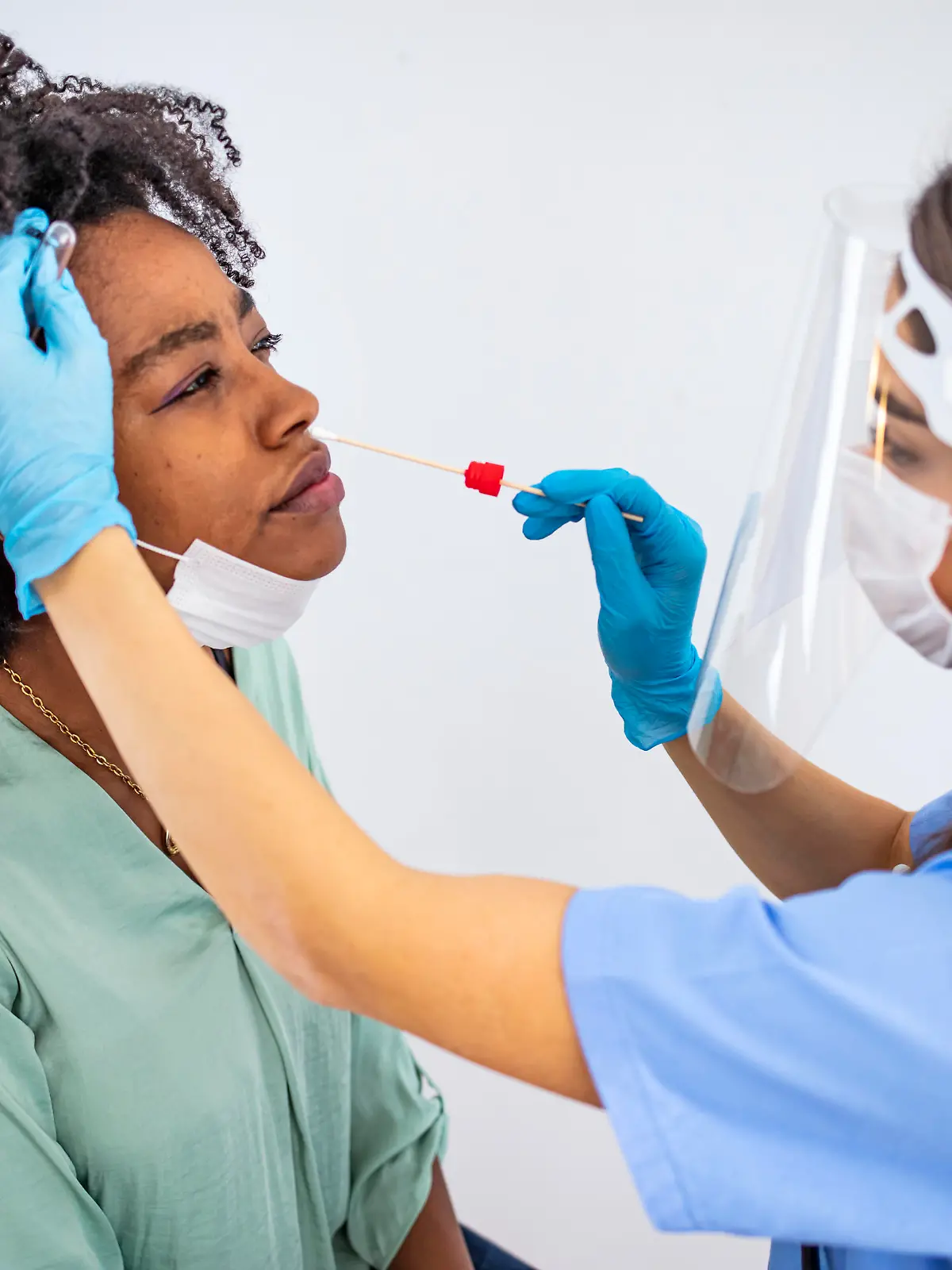 Shot of a doctor using cotton swab while doing coronavirus PCR test at the hospital. Doctor laboratory assistant takes swab from nose of sick patient. Coronavirus sample from female patient's nose or mouth.