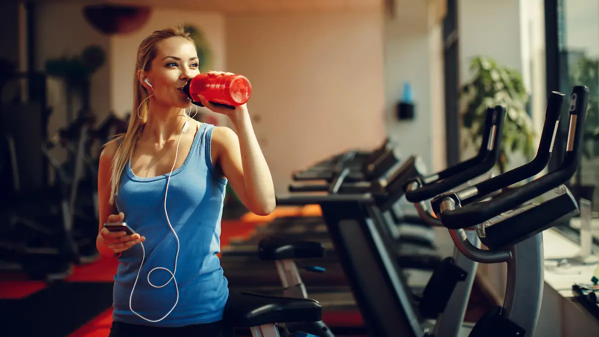 Beautiful young woman resting and drinking water in the gym