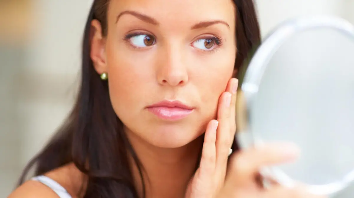 Closeup portrait of young woman holding a mirror