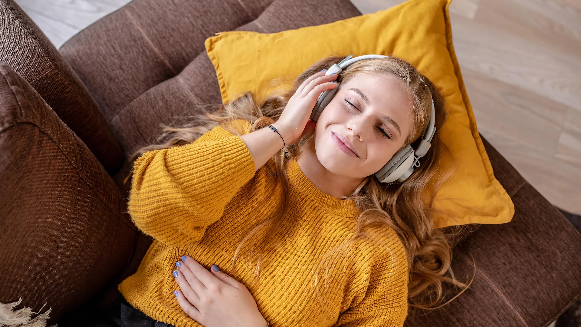 Photo of young woman with headphones laying on the couch and smiling