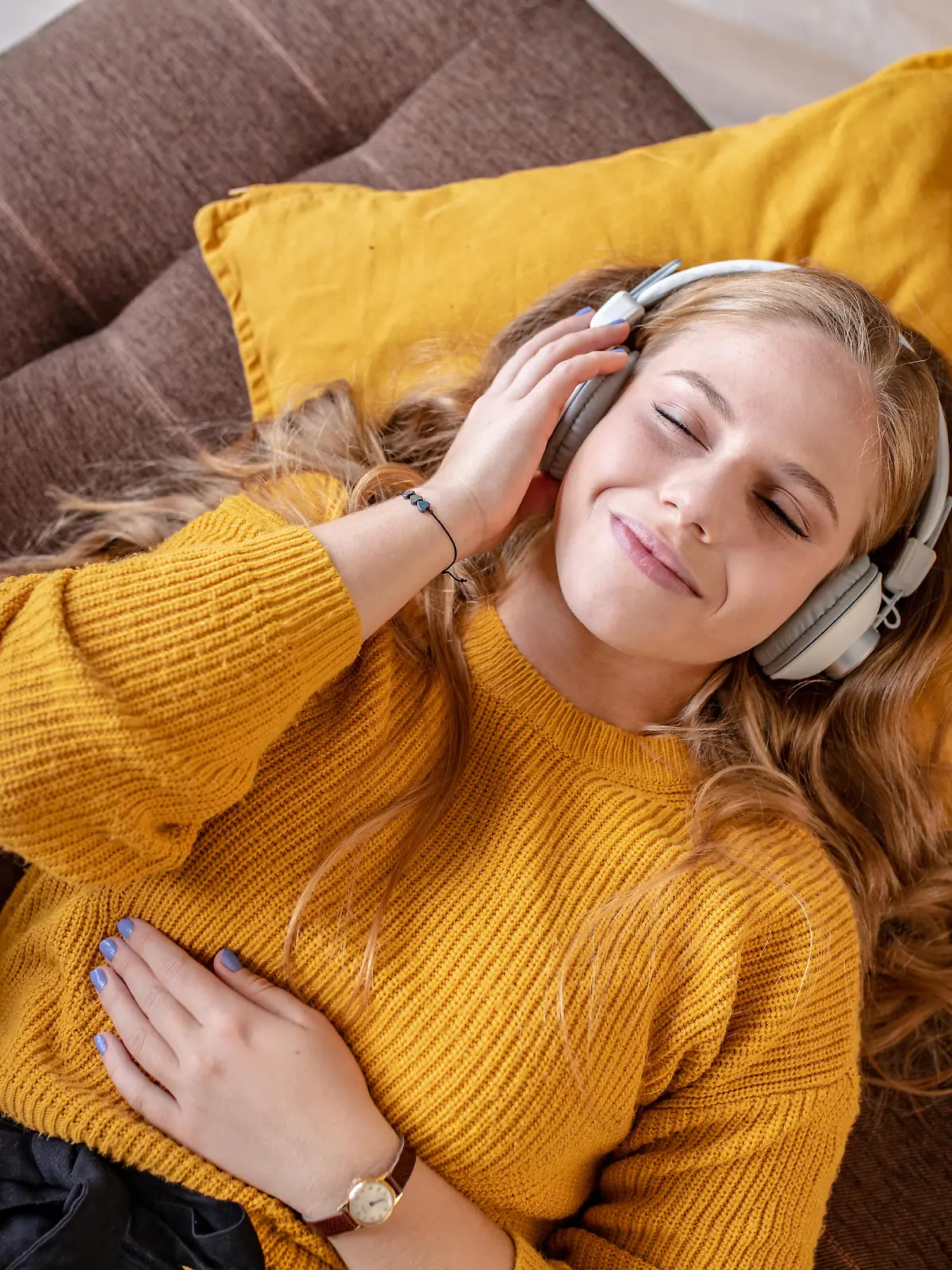 Photo of young woman with headphones laying on the couch and smiling