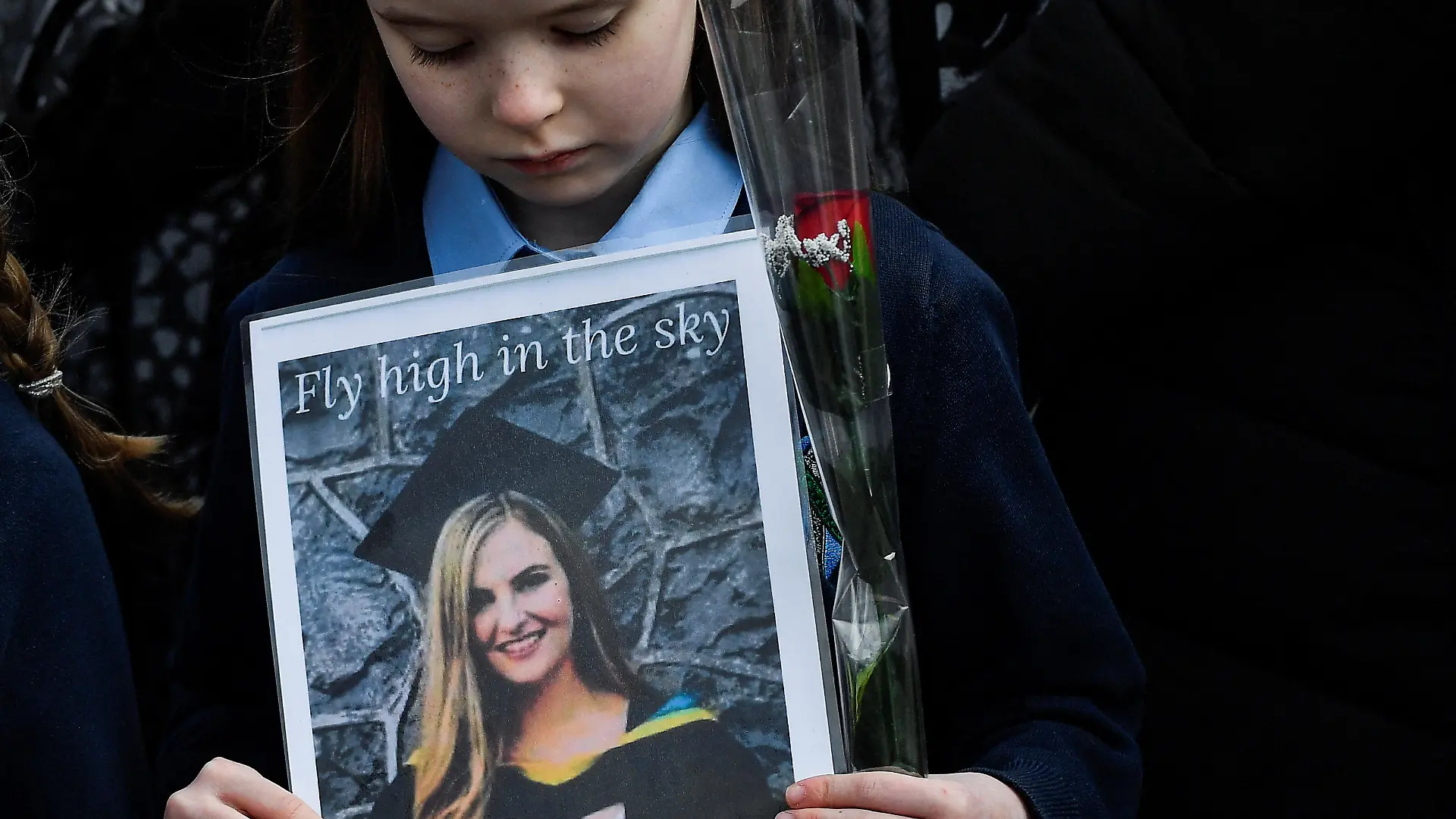 A girl of a guard of honour of the children whom 23-year-old teacher, Ashling Murphy who was murdered while out jogging, taught at Durrow National School looks down at a picture of the teacher she holds while people gather for her funeral by the St Brigid's Church in Mountbolus near Tullamore, Ireland January 18, 2022. REUTERS/Clodagh Kilcoyne