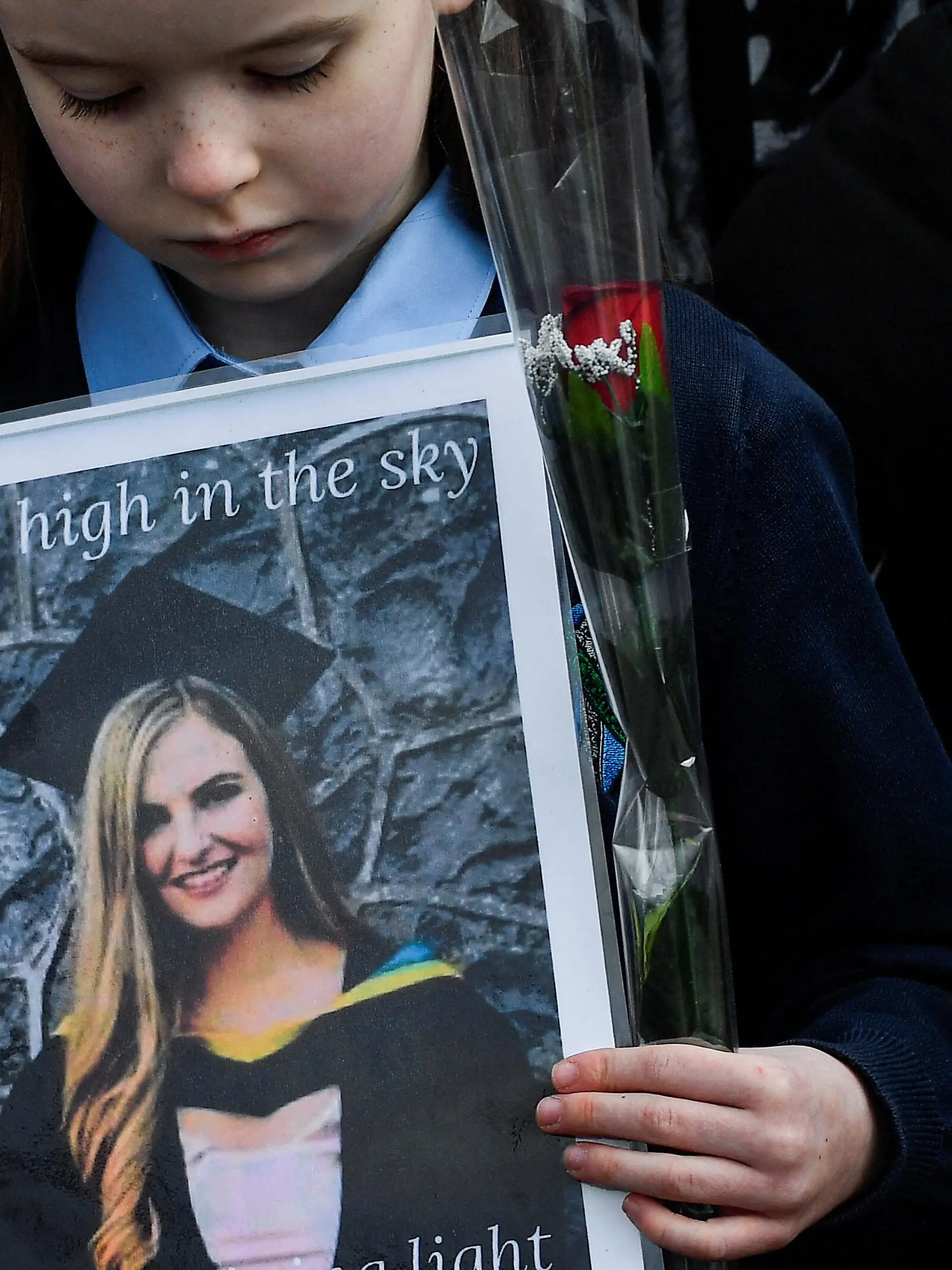 A girl of a guard of honour of the children whom 23-year-old teacher, Ashling Murphy who was murdered while out jogging, taught at Durrow National School looks down at a picture of the teacher she holds while people gather for her funeral by the St Brigid's Church in Mountbolus near Tullamore, Ireland January 18, 2022. REUTERS/Clodagh Kilcoyne