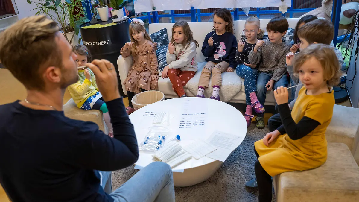 11.01.2022, Bayern, Augsburg: Unter Anleitung eines Kindergärtners machen die Kinder in einer Kindertagesstätte am Vormittag eine Corona-Pooltestung (Lollitest), die nun regelmäßig durchgeführt werden soll. Am Montag, 10.01.2022 haben in Bayern die Schulen und auch die meisten Kindertagesstätten wieder geöffnet - mit Änderungen bei den Vorgaben zu Corona-Tests für Krippen- und Kindergartenkinder. Foto: Peter Kneffel/dpa - ACHTUNG: Nur zur redaktionellen Verwendung im Zusammenhang mit einer Berichterstattung über diesen Termin und nur mit vollständiger Nennung des vorstehenden Credits +++ dpa-Bildfunk +++