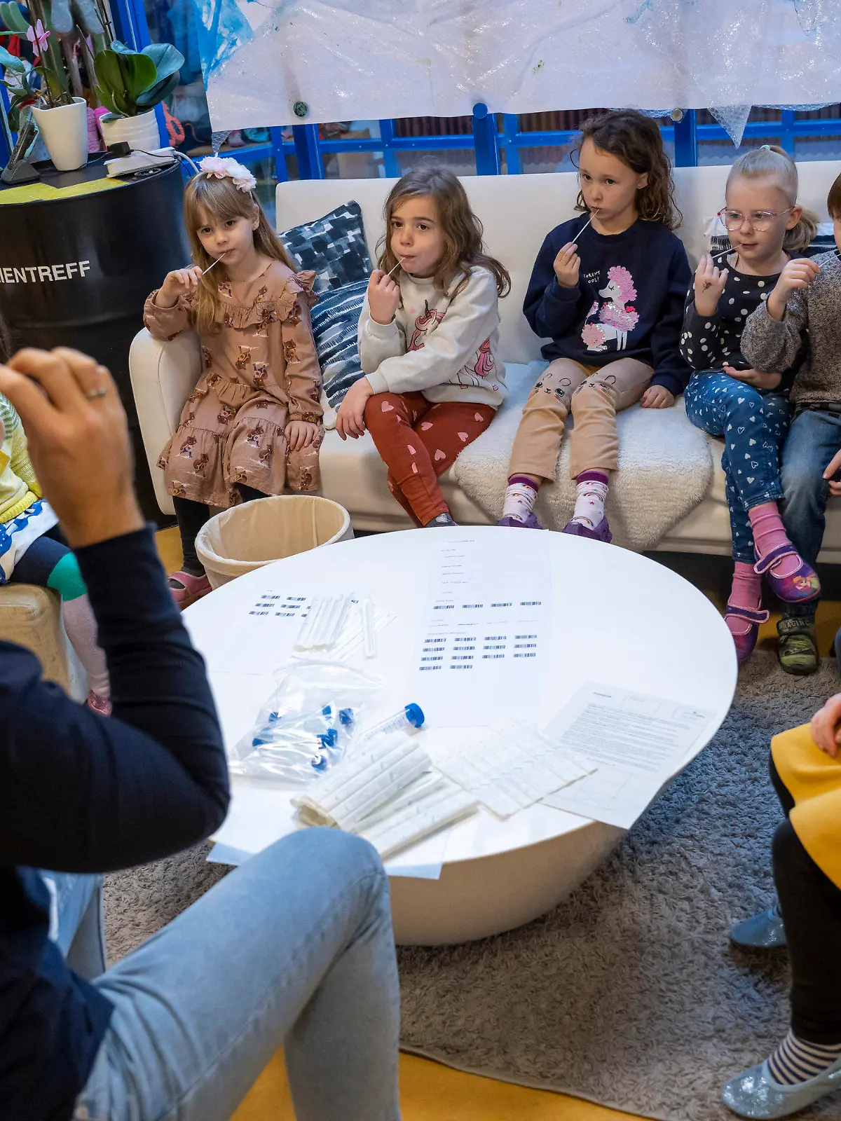 11.01.2022, Bayern, Augsburg: Unter Anleitung eines Kindergärtners machen die Kinder in einer Kindertagesstätte am Vormittag eine Corona-Pooltestung (Lollitest), die nun regelmäßig durchgeführt werden soll. Am Montag, 10.01.2022 haben in Bayern die Schulen und auch die meisten Kindertagesstätten wieder geöffnet - mit Änderungen bei den Vorgaben zu Corona-Tests für Krippen- und Kindergartenkinder. Foto: Peter Kneffel/dpa - ACHTUNG: Nur zur redaktionellen Verwendung im Zusammenhang mit einer Berichterstattung über diesen Termin und nur mit vollständiger Nennung des vorstehenden Credits +++ dpa-Bildfunk +++