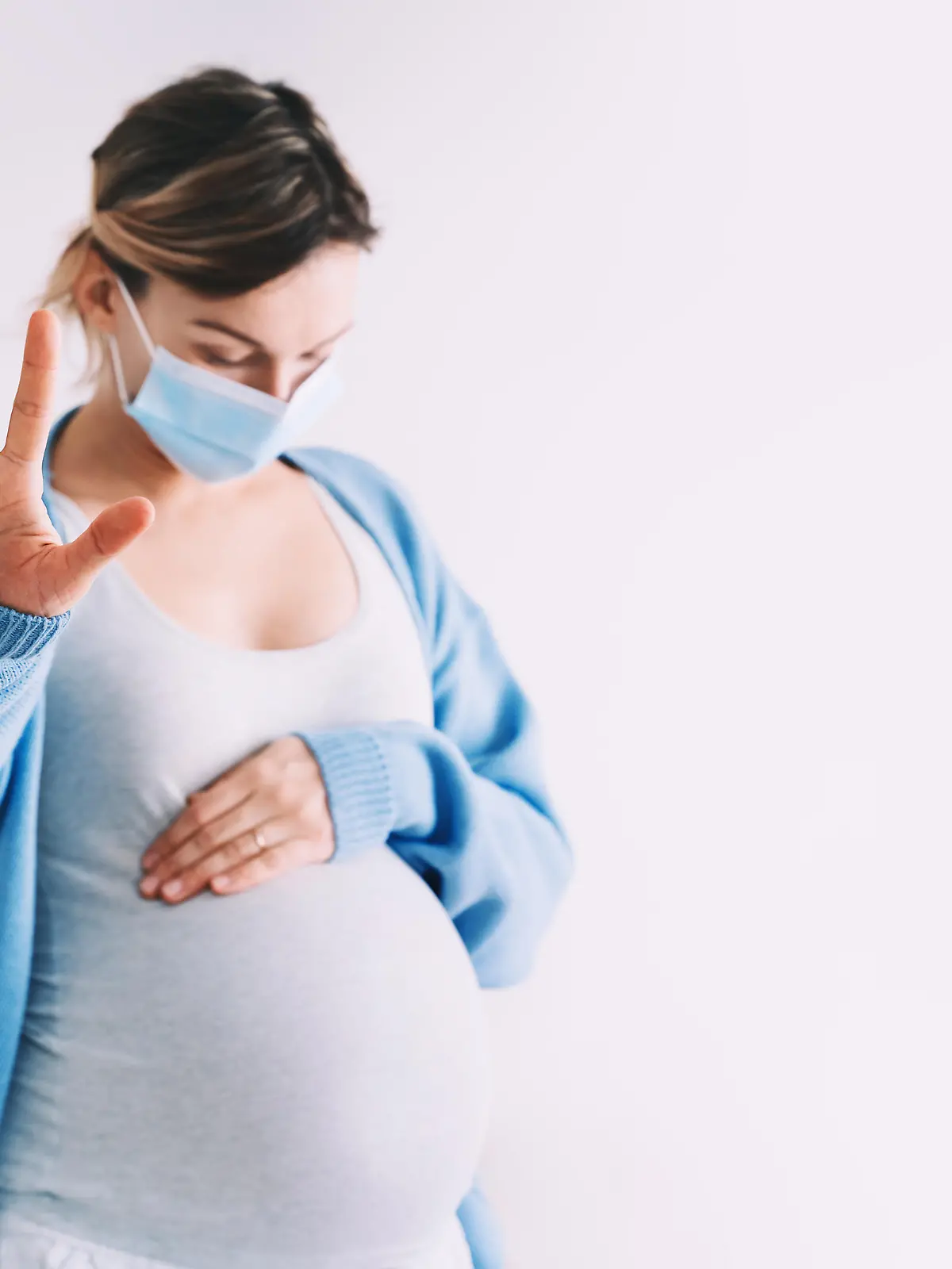 Pregnancy and childbirth during Infections. Pregnant woman in medical mask hugging belly showing STOP gesture. Protection and prevention during viruses, mother care of her and unborn baby health.
