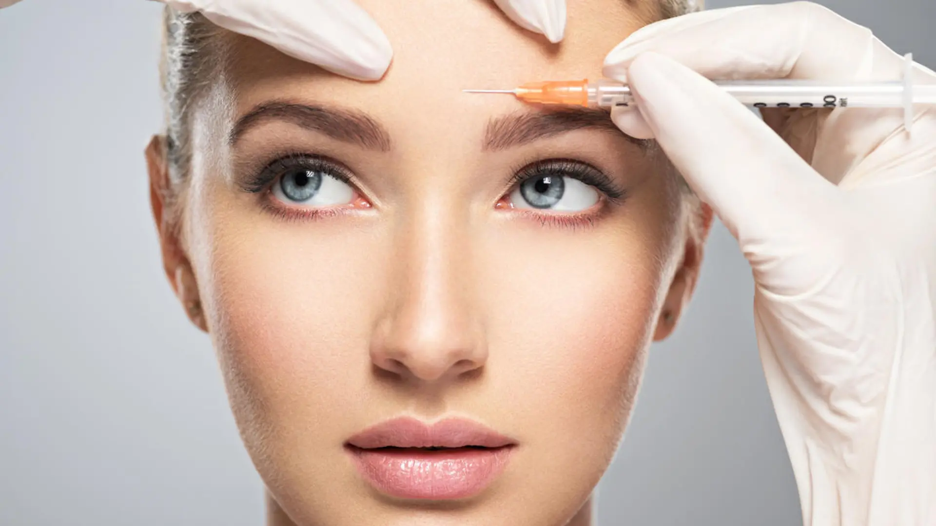 Portrait of young Caucasian woman getting botox cosmetic injection in forehead. Beautiful woman gets botox injection in her face.