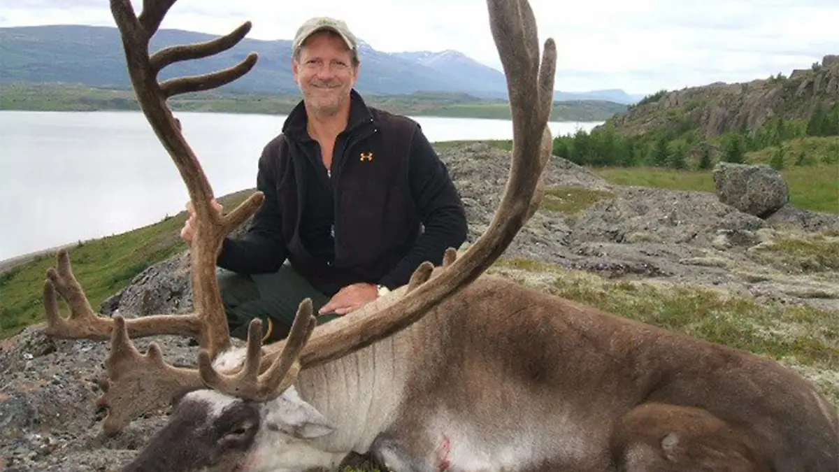 Mann mit totem Hirsch schaut lachend in die Kamera