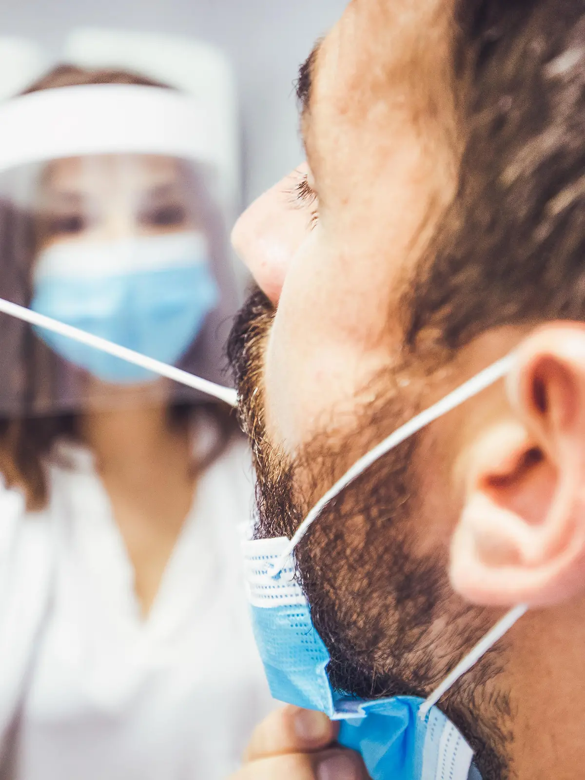 A rear view of a man's head while a doctor is taking a sample of his swab. Both protected with face masks.