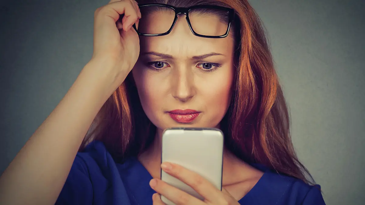 Closeup portrait headshot young woman with glasses having trouble seeing cell phone has vision problems. Bad text message. Negative human emotion facial expression perception. Confusing technology