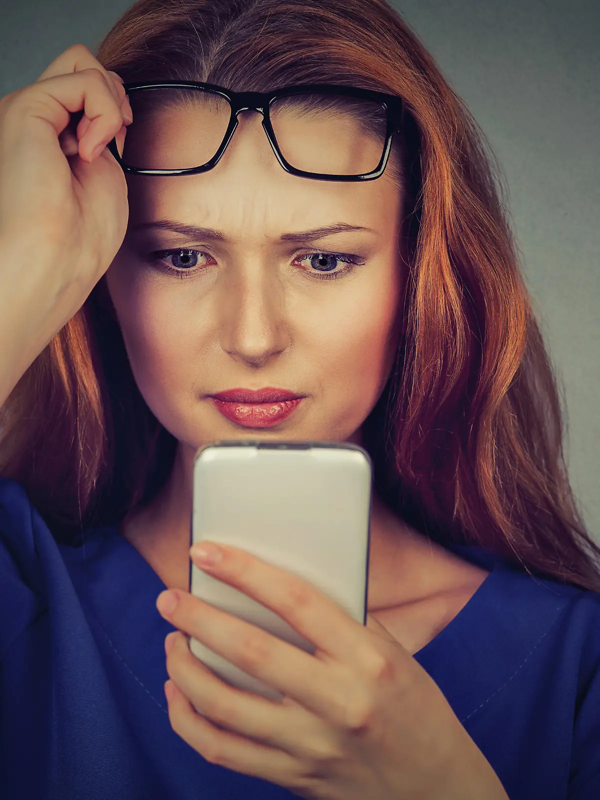 Closeup portrait headshot young woman with glasses having trouble seeing cell phone has vision problems. Bad text message. Negative human emotion facial expression perception. Confusing technology