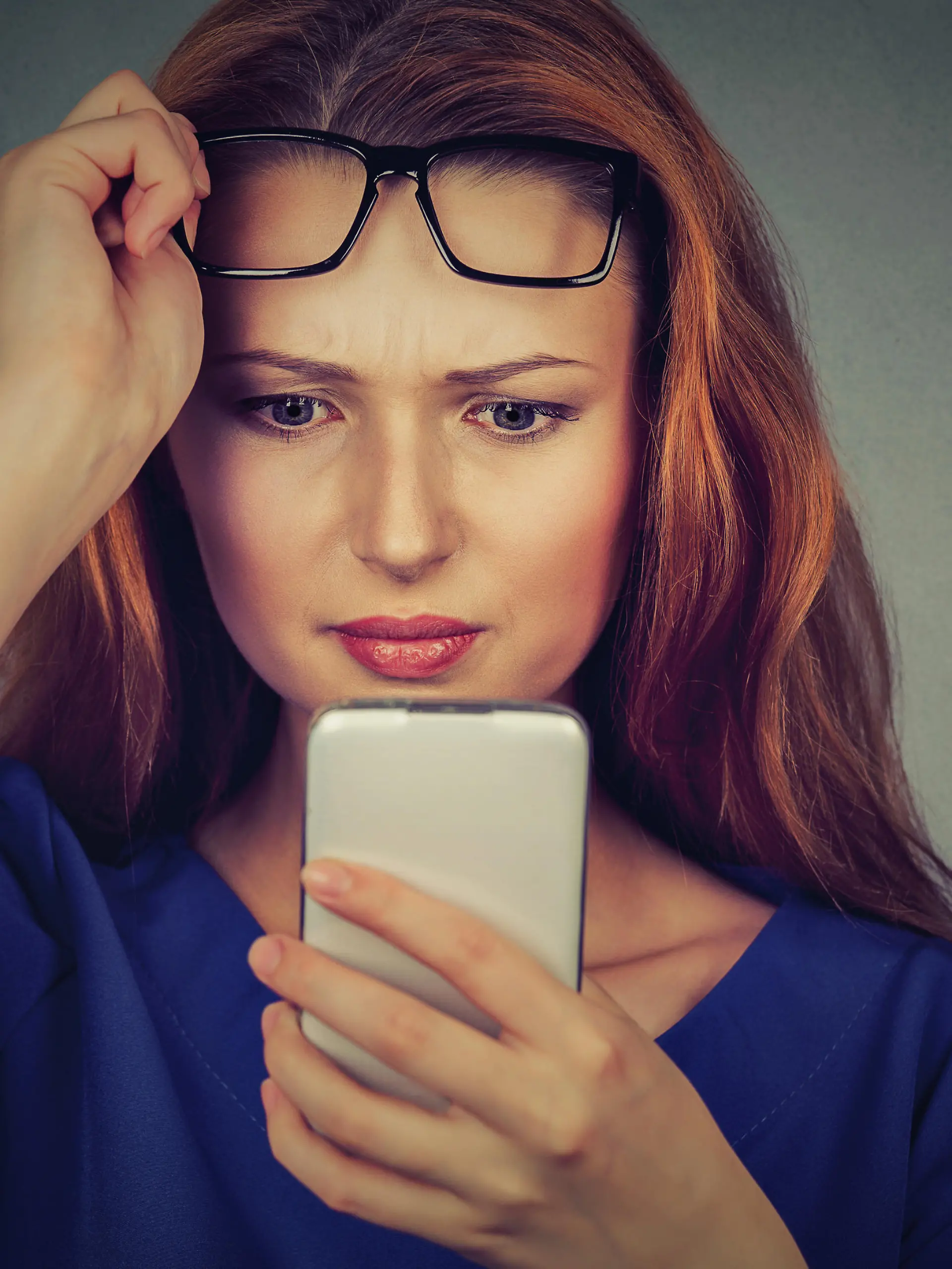 Closeup portrait headshot young woman with glasses having trouble seeing cell phone has vision problems. Bad text message. Negative human emotion facial expression perception. Confusing technology