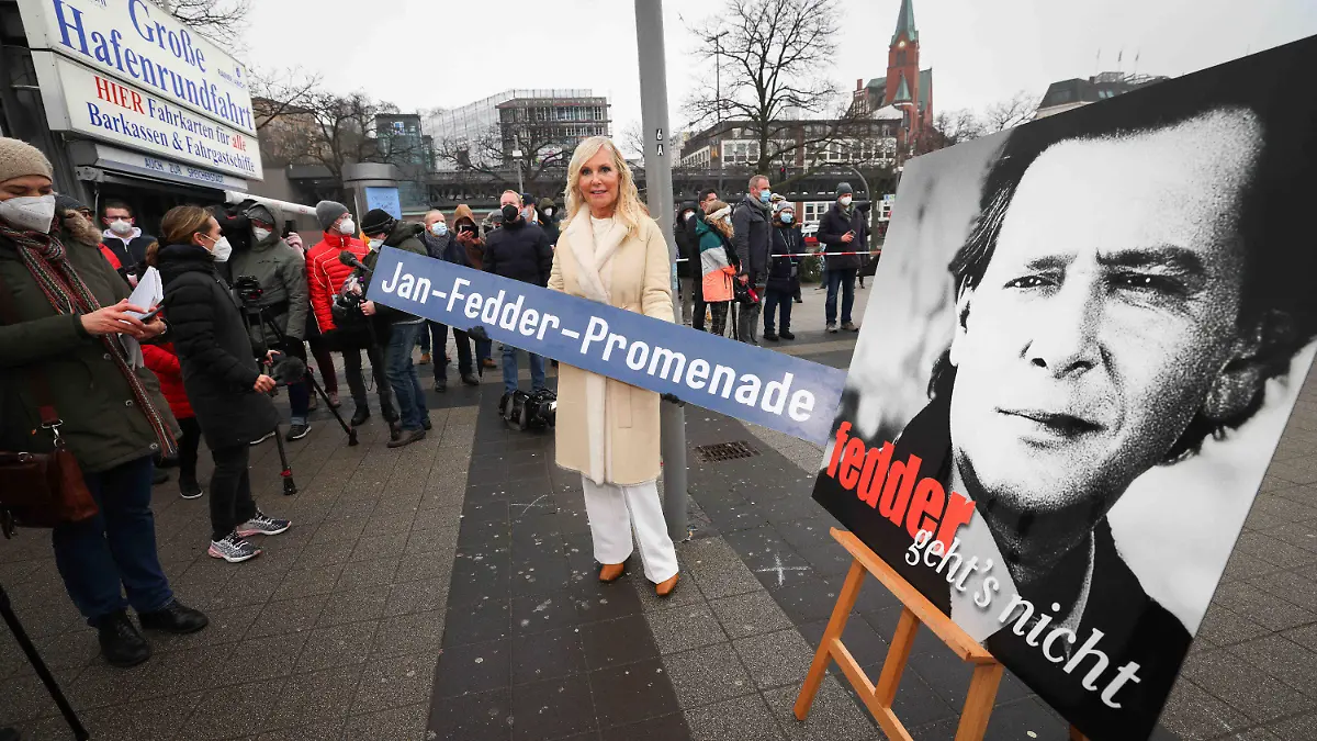14.01.2022, Hamburg: Marion Fedder (M), Witwe von Jan Fedder, hält ein Schild mit dem Text «Jan-Fedder-Promenade» bei der Einweihung der Jan-Fedder-Promenade an den Landungsbrücken. Die Elbpromenade zwischen Landungsbrücken und Baumwall wurde am Freitag nach dem 2019 gestorbenen Hamburger Volksschauspieler benannt. Foto: Christian Charisius/dpa +++ dpa-Bildfunk +++