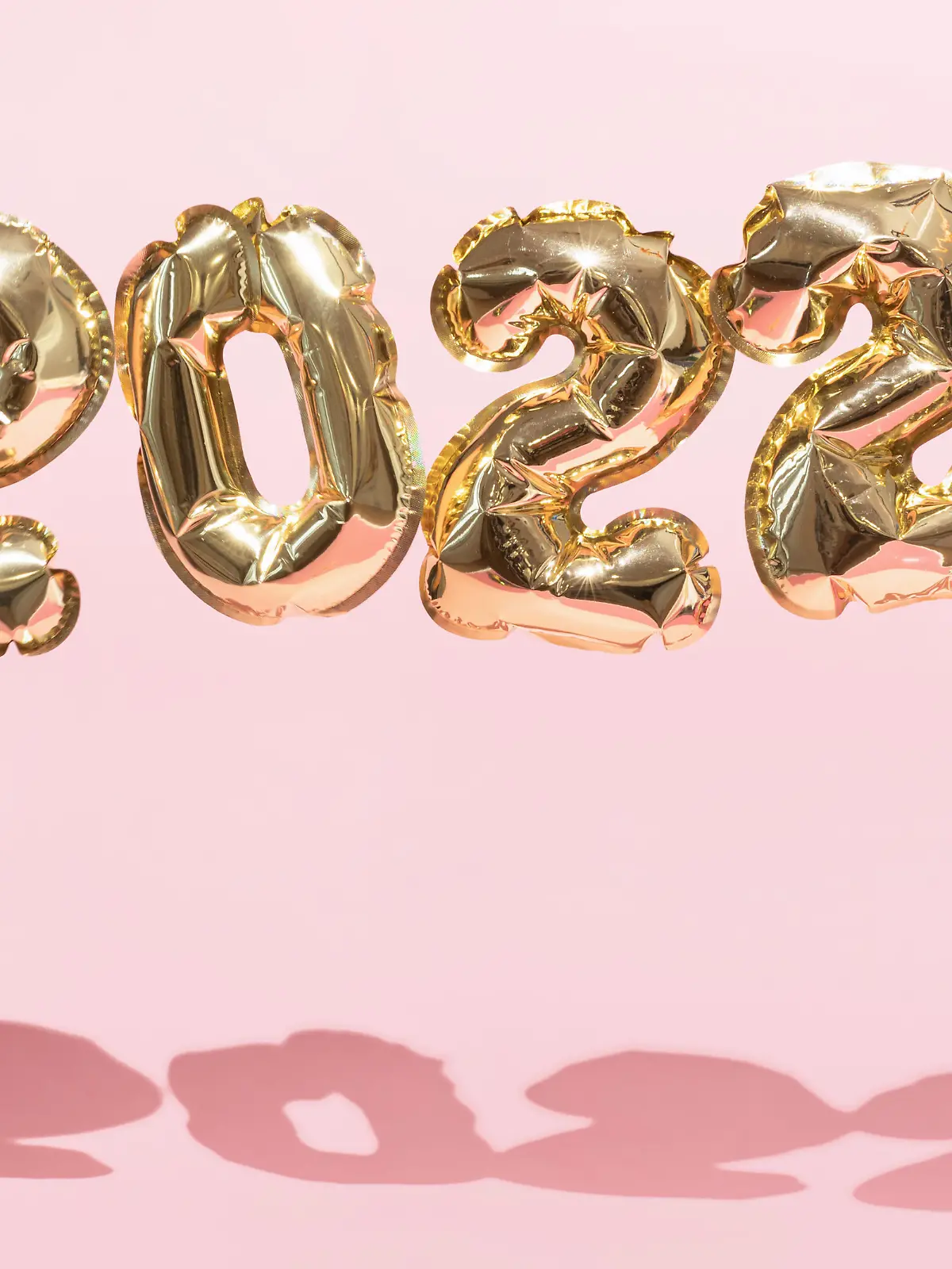 Gold 2022 balloons on a pink background with confetti and Christmas shiny balls, flat lay. New Years celebration concept