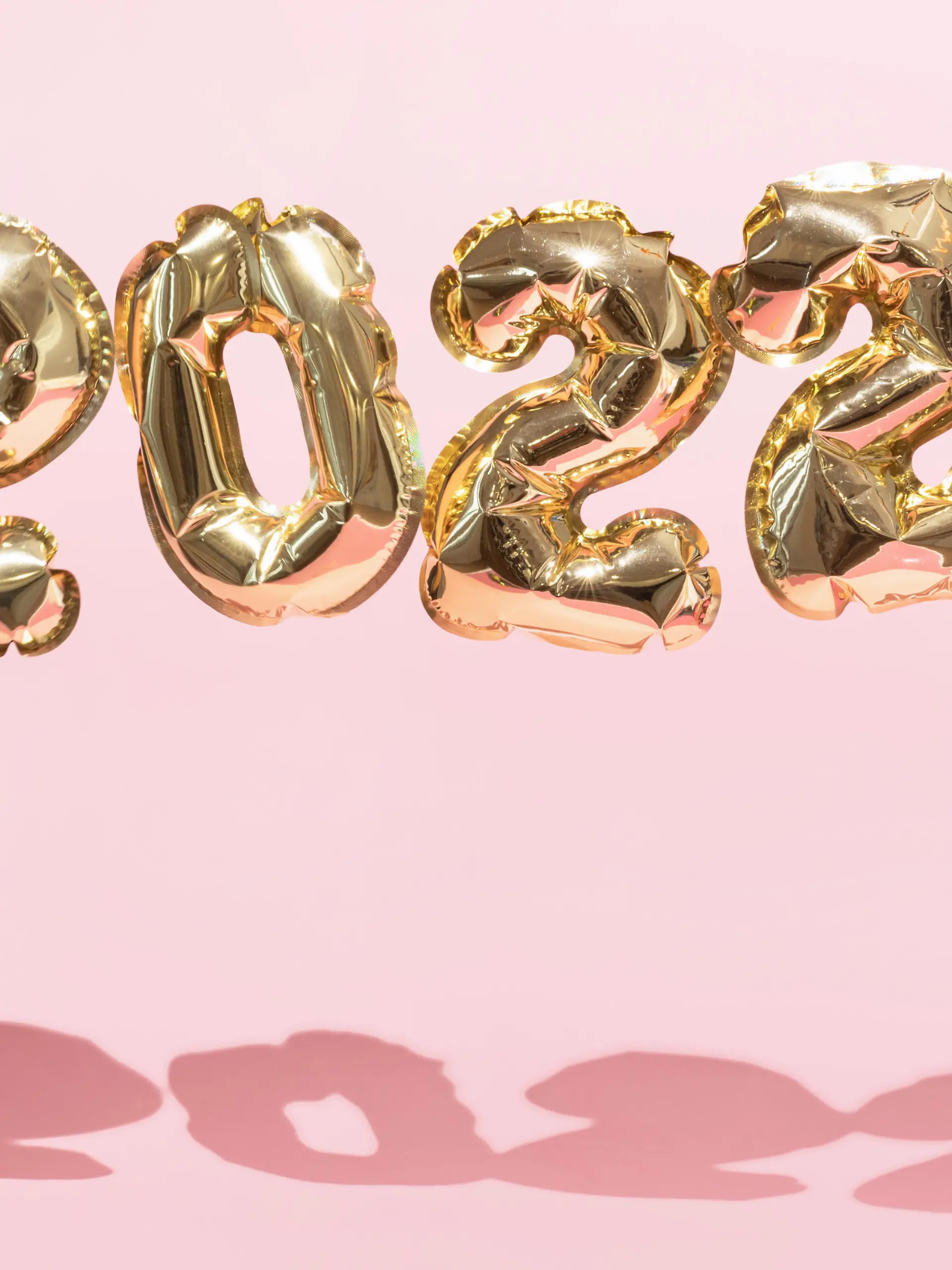 Gold 2022 balloons on a pink background with confetti and Christmas shiny balls, flat lay. New Years celebration concept