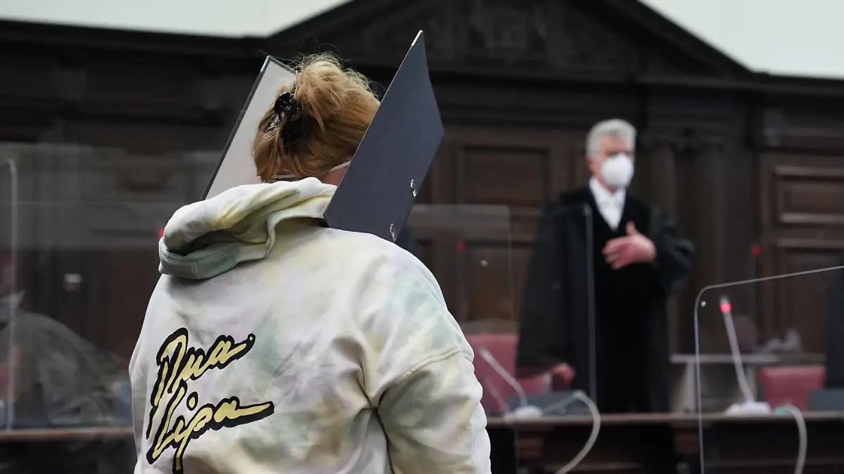 13.01.2022, Hamburg: Die Angeklagte steht zu Beginn des Prozesses wegen Mitgliedschaft in einer terroristischen Vereinigung im Ausland im Sitzungssaal im Strafjustizgebäude. Im Hintergrund steht Norbert Sakuth, Vorsitzender Richter am Oberlandesgericht. Die Deutsche aus Bad Oldesloe soll im Sommer 2016 mit ihrem damals 13-jährigen Sohn nach Syrien gereist und sich der Terrormiliz Islamischer Staat (IS) angeschlossen haben. Knapp zwei Jahre später kam der Sohn bei einem Bombenangriff ums Leben. Der Familienvater soll bereits 2015 als Kämpfer zum IS nach Syrien gegangen sein. Foto: Marcus Brandt/dpa +++ dpa-Bildfunk +++