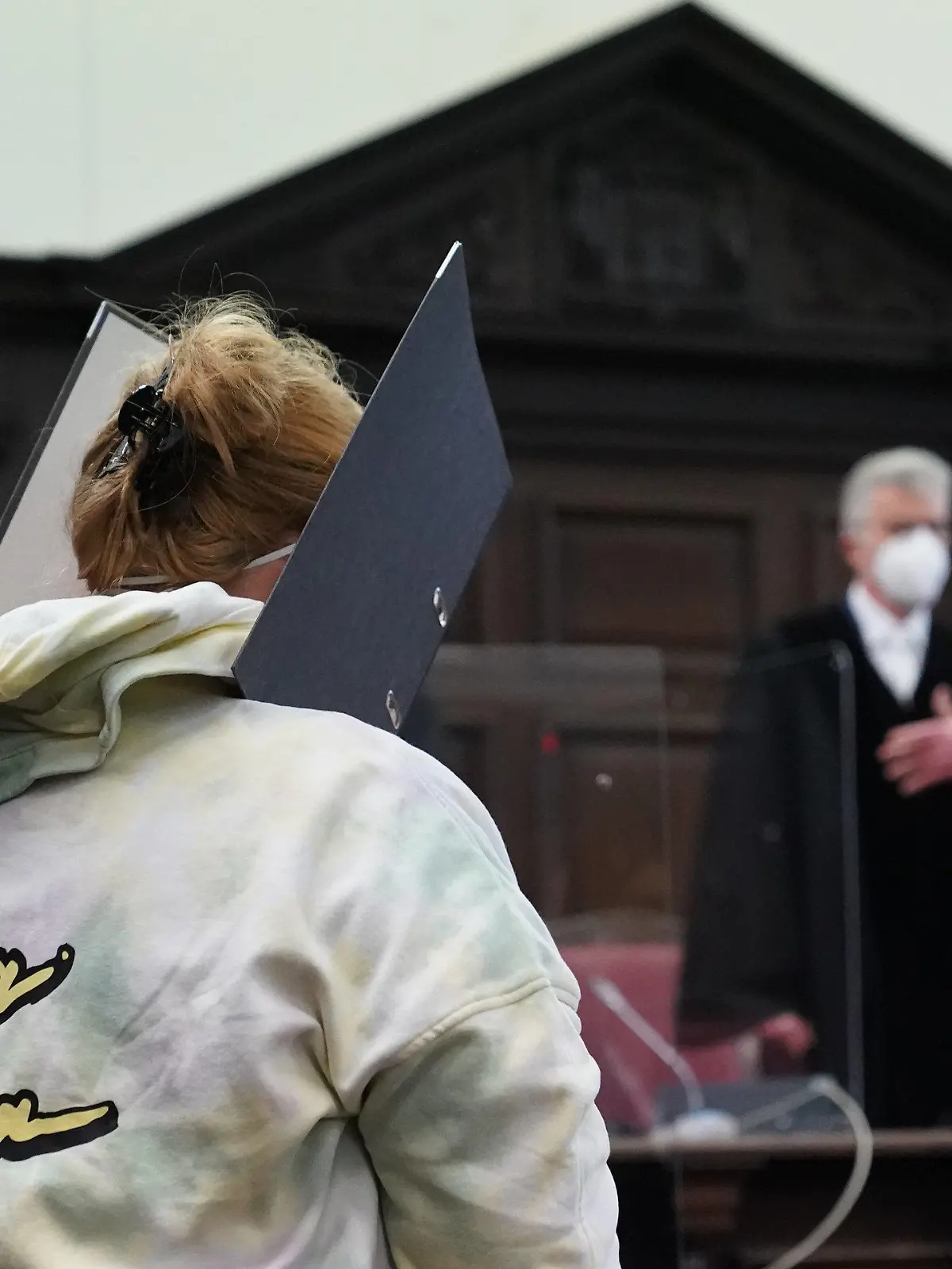 13.01.2022, Hamburg: Die Angeklagte steht zu Beginn des Prozesses wegen Mitgliedschaft in einer terroristischen Vereinigung im Ausland im Sitzungssaal im Strafjustizgebäude. Im Hintergrund steht Norbert Sakuth, Vorsitzender Richter am Oberlandesgericht. Die Deutsche aus Bad Oldesloe soll im Sommer 2016 mit ihrem damals 13-jährigen Sohn nach Syrien gereist und sich der Terrormiliz Islamischer Staat (IS) angeschlossen haben. Knapp zwei Jahre später kam der Sohn bei einem Bombenangriff ums Leben. Der Familienvater soll bereits 2015 als Kämpfer zum IS nach Syrien gegangen sein. Foto: Marcus Brandt/dpa +++ dpa-Bildfunk +++