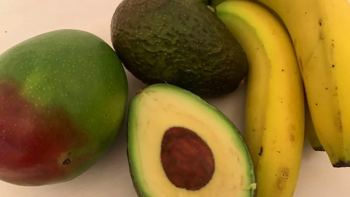 eine aufgeschnittene Avocado, Banane und Mango liegen auf einer Oberfläche.