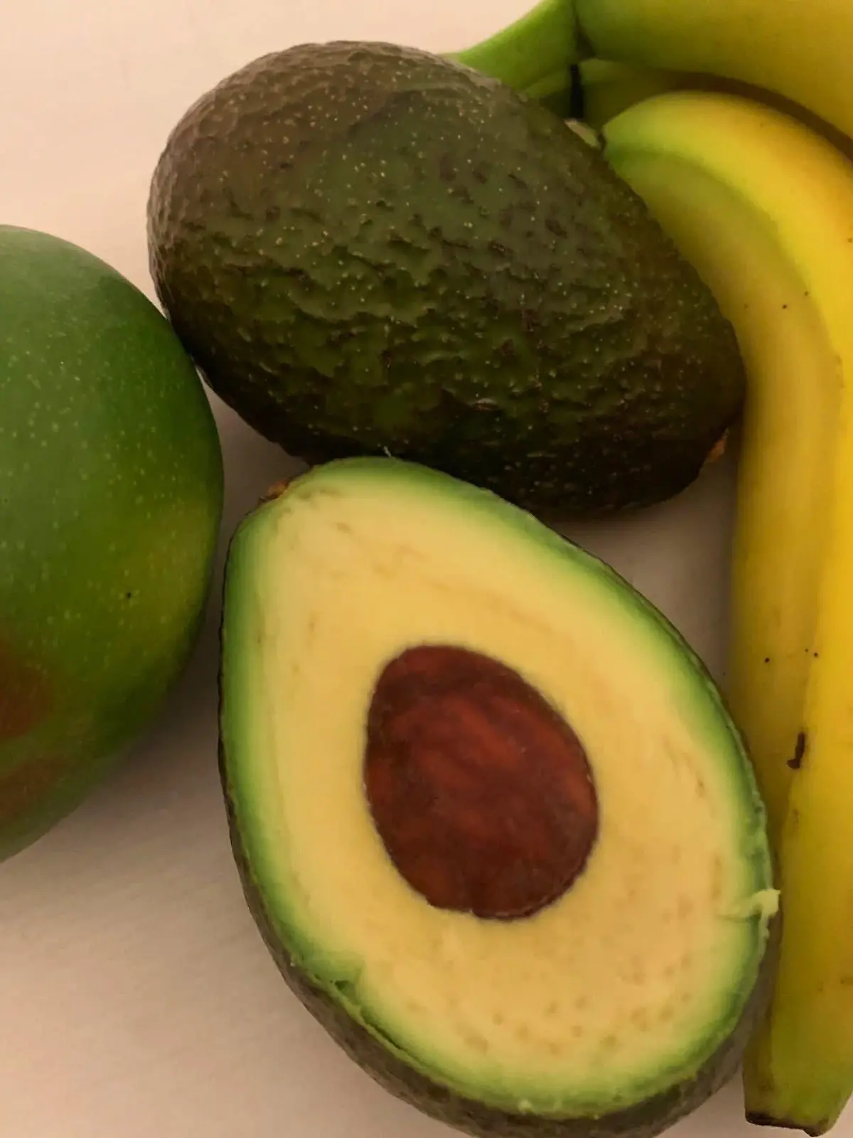 eine aufgeschnittene Avocado, Banane und Mango liegen auf einer Oberfläche.