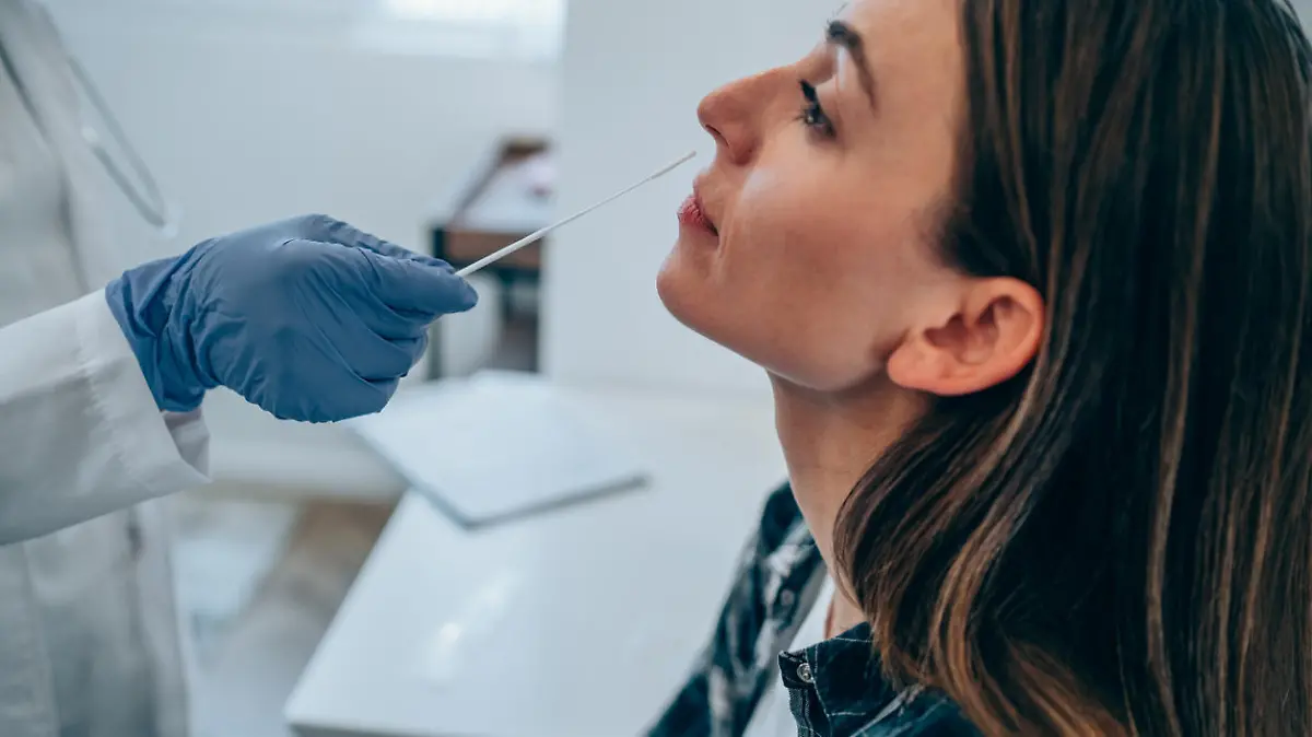 Shot of a doctor using cotton swab while doing coronavirus PCR test at the hospital. Doctor laboratory assistant takes swab from nose of sick patient. Unrecognizable doctor with protective glove taking coronavirus sample from female patient's nose.