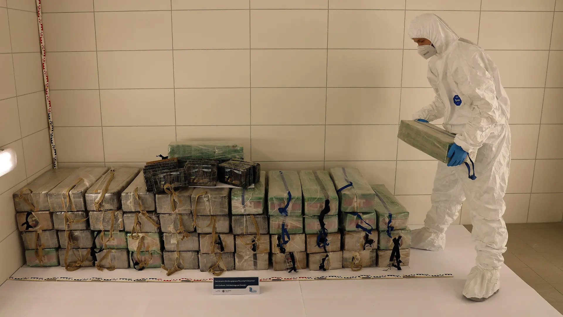 HANDOUT - 11.01.2022, Sachsen, Dresden: Ein Mann stapelt in Plastiktüten verpacktes Kokain in einem Raum. In einer Zuckerlieferung sind in Sachsen 700 Kilogramm Kokain entdeckt worden. Der Straßenverkaufswert der Drogen liege im dreistelligen Millionenbereich, es sei der bisher größte Kokain-Fund im Freistaat, teilten das Landeskriminalamt Sachsen und das Zollfahndungsamt Dresden am Dienstag mit. Foto: -/LKA Sachsen/dpa - ACHTUNG: Nur zur redaktionellen Verwendung im Zusammenhang mit der aktuellen Berichterstattung und nur mit vollständiger Nennung des vorstehenden Credits +++ dpa-Bildfunk +++