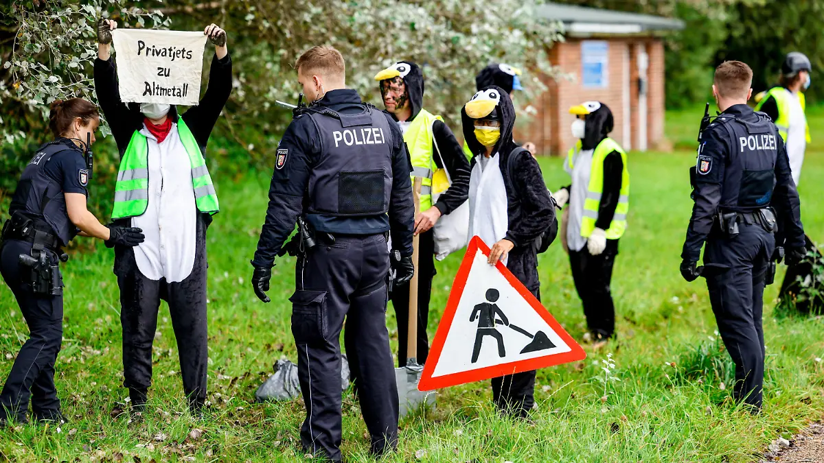 25.08.2023, Schleswig-Holstein, Tinnum/Sylt: Als Pinguine verkleidete Aktivistin der Gruppe ·Am Boden bleiben· werden von Polizisten überprüft, nachdem die Gruppe versucht hat den Flughafen auf Sylt zu blockieren. Foto: Axel Heimken/dpa +++ dpa-Bildfunk +++