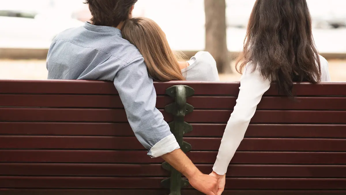 Love Triangle. Cheating Boyfriend Hugging Girlfriend Holding Hands With Her Girl Friend Sitting On Bench Together In Park Outdoor. Back-View