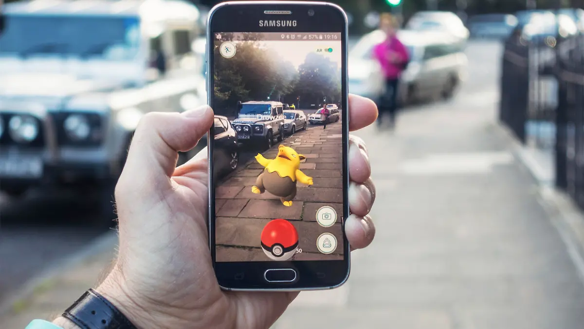 Edinburgh, UK - July 18, 2016: Closeup of a man holding a Samsung S6 smartphone, playing Pokemon Go with the game's augmented reality superimposing a character onto the pavement surface, as a person approaches in the distance.