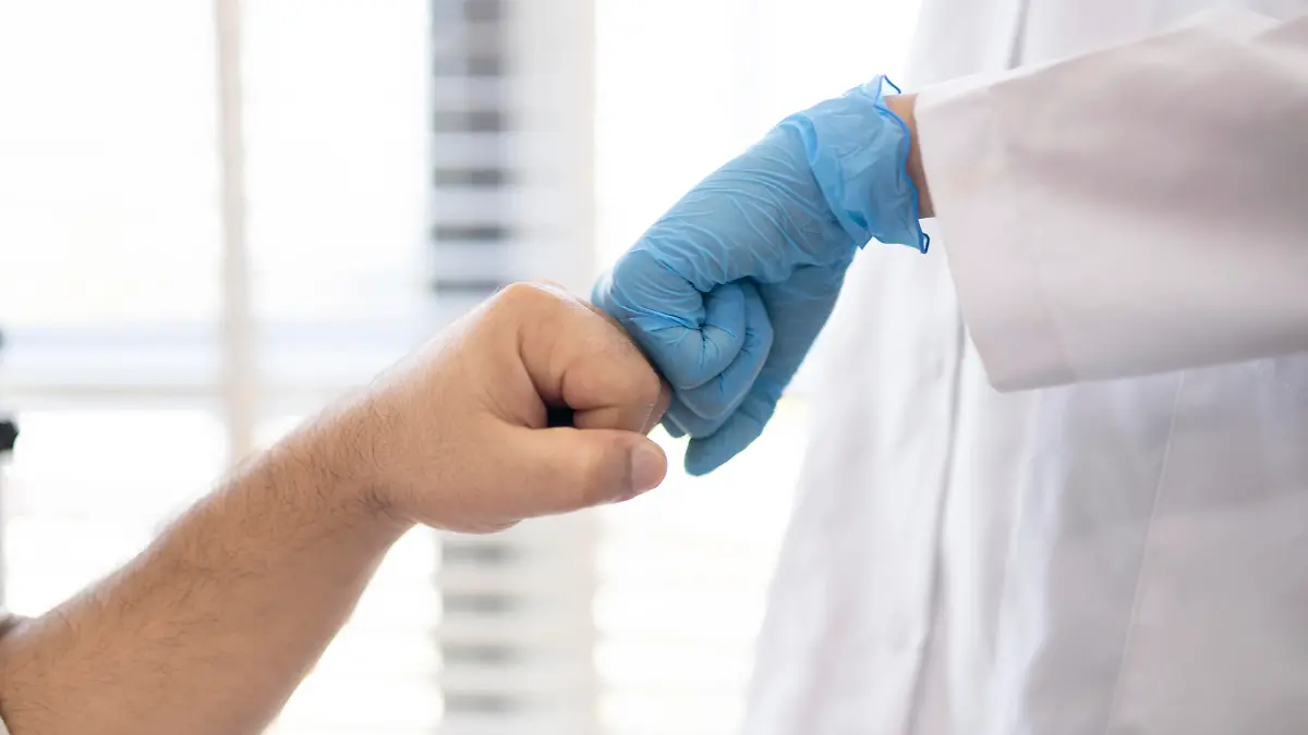Doctor's hand with blue gloves are touching patient's hand. She is explaining something.