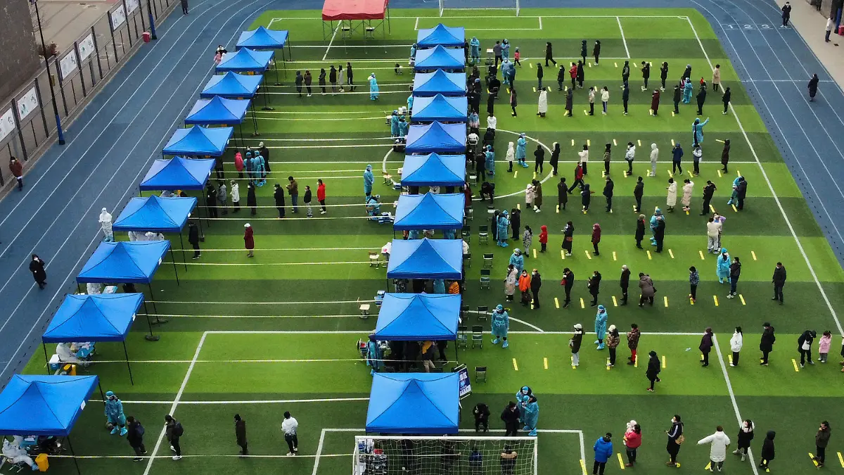 09.01.2022, China, Tianjin: Einwohner stehen auf einem Fußballfeld für einen Corona-Test während eines Massentests Schlange. Tianjin, eine chinesische Großstadt in der Nähe von Peking, hat ihre 14 Millionen Einwohner teilweise abgeriegelt, nachdem 41 Kinder und Erwachsene positiv auf Corona getestet wurden, darunter mindestens zwei mit der Omikron-Variante. Foto: Sun Fanyue/Xinhua/AP/dpa - ACHTUNG: Nur zur redaktionellen Verwendung und nur mit vollständiger Nennung des vorstehenden Credits +++ dpa-Bildfunk +++