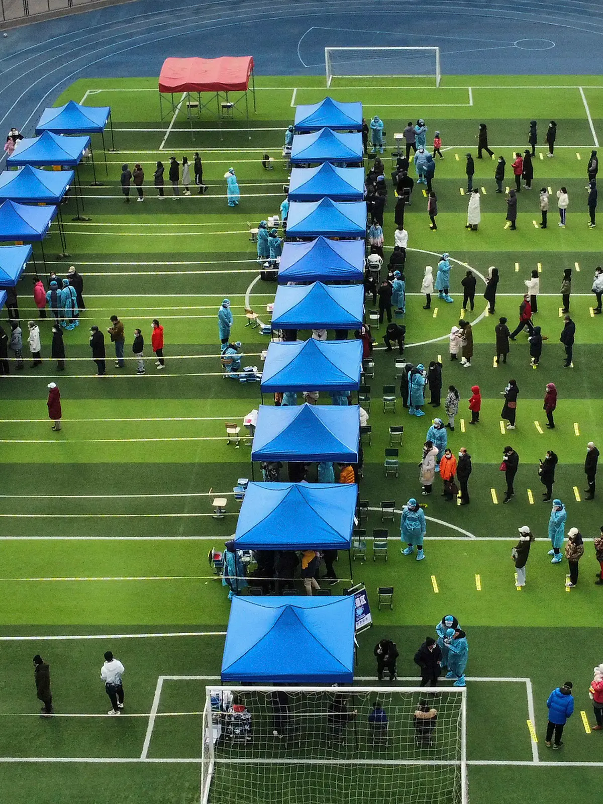 09.01.2022, China, Tianjin: Einwohner stehen auf einem Fußballfeld für einen Corona-Test während eines Massentests Schlange. Tianjin, eine chinesische Großstadt in der Nähe von Peking, hat ihre 14 Millionen Einwohner teilweise abgeriegelt, nachdem 41 Kinder und Erwachsene positiv auf Corona getestet wurden, darunter mindestens zwei mit der Omikron-Variante. Foto: Sun Fanyue/Xinhua/AP/dpa - ACHTUNG: Nur zur redaktionellen Verwendung und nur mit vollständiger Nennung des vorstehenden Credits +++ dpa-Bildfunk +++