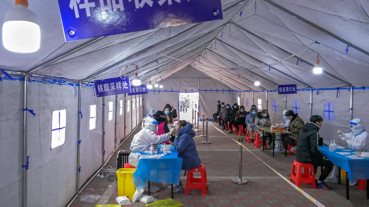 09.01.2022, China, Tianjin: Einwohner mit Mund-Nasen-Schutz werden während eines Massentests in einem Zelt auf das Coronavirus getestet. Nach dem Auftreten der ersten lokalen Omikron-Fälle in China hat die nordostchinesische Stadt Tianjin Massentests für die gesamte Bevölkerung angeordnet. Tianjin ist eine Nachbarstadt von Peking, wo am 04.02.2022 die Olympischen Winterspiele beginnen sollen. Foto: Uncredited/CHINATOPIX/AP/dpa +++ dpa-Bildfunk +++