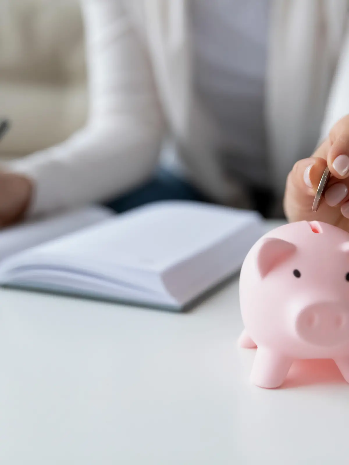 Thrifty woman sit at table hold pen writing daily expenses in diary put coin in pink piggy bank close up. Saving money for future, caring for tomorrow, makes stash of cash, investment, economy concept