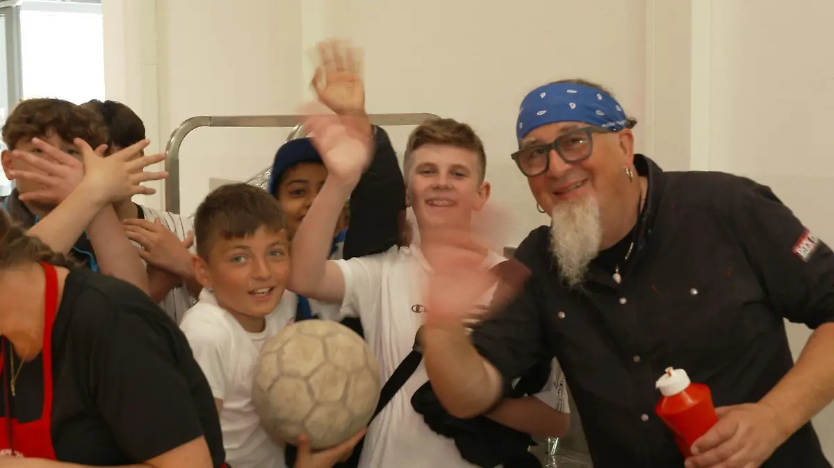 Schüler der Stadtteilschule Wilhelmsburg und TV-Koch Stefan Marquard winken in die Kamera.
