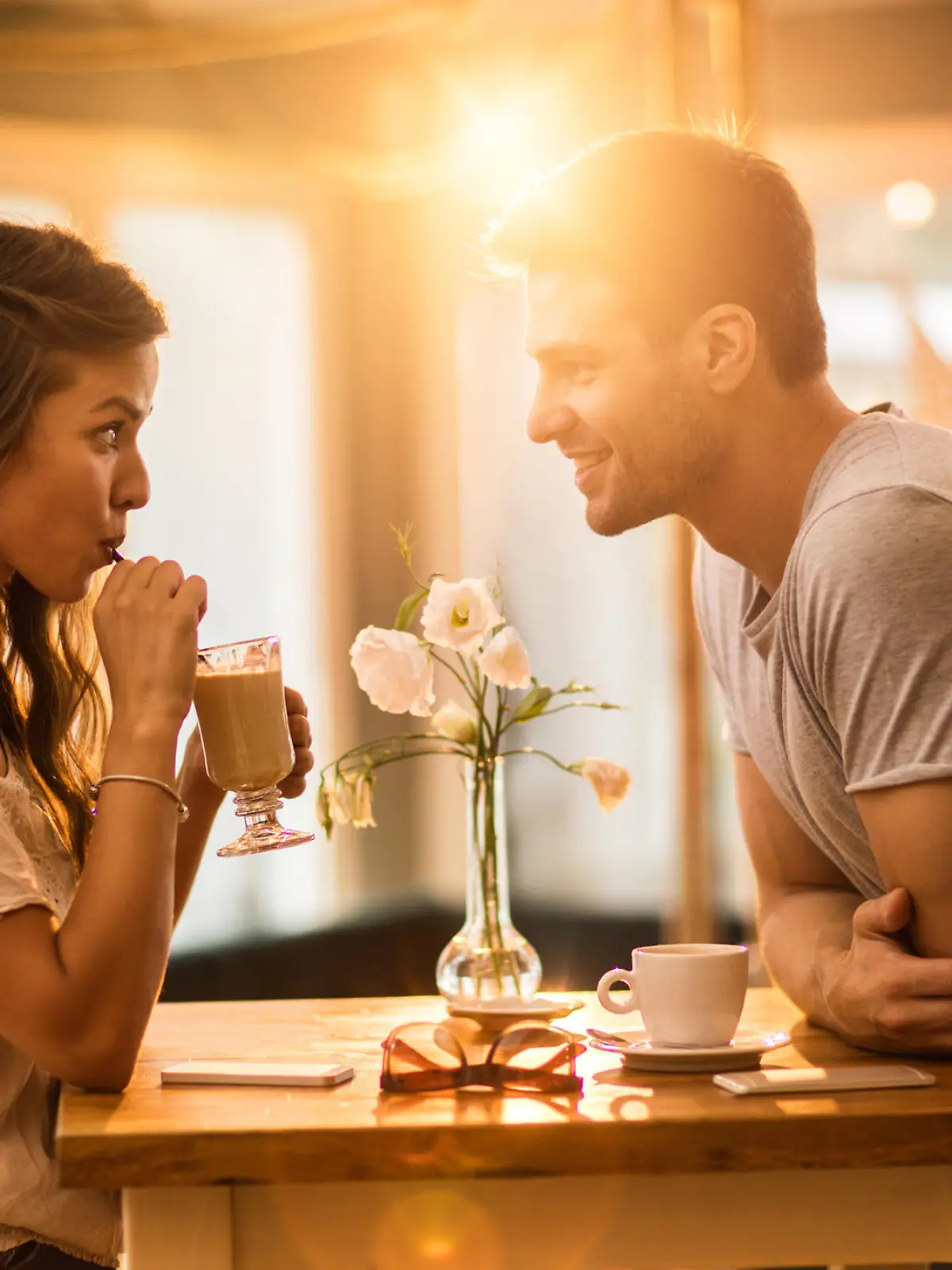 Young woman drinking coffee and communicating with her smiling boyfriend in a cafe.