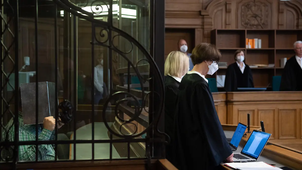 10.08.2021, Berlin: Der Angeklagte (l) sitzt in einem Gerichtssaal und hält sich eine Pappe vor dem Gesicht. Der 41 Jahre alte Lehrer muss sich wegen mutmaßlichem Mord verantworten. Der Beschuldigte soll einen 43-jährigen Mann, den er kurz zuvor über ein Dating-Portal kennengelernt hatte, in seiner Wohnung getötet haben. Dann soll er das Opfer zerteilt und die Leichenteile an verschiedenen Orten in Berlin abgelegt haben. Die Staatsanwaltschaft geht von einer "sadistisch-kannibalistisch geprägten sexuellen Tatmotivation" aus. Foto: Paul Zinken/dpa +++ dpa-Bildfunk +++