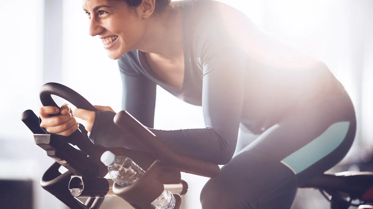 Happy athletic woman cycling on exercise bike in a gym.